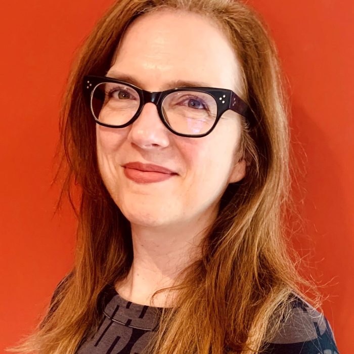 Photo of Robbyn wearing glasses on a burnt orange backdrop